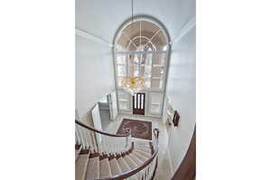 Entryway with a chandelier, crown molding, vaulted ceiling, and stairs