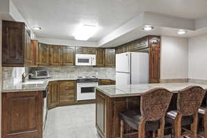 Kitchen with a peninsula, white appliances, a breakfast bar, a sink, and decorative backsplash