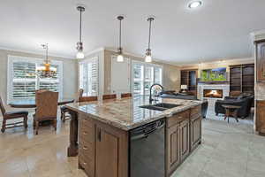 Kitchen featuring a sink, a lit fireplace, dishwasher, a center island with sink, and crown molding