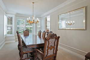 Carpeted dining space with baseboards, ornamental molding, and an inviting chandelier