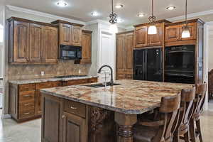 Kitchen with decorative backsplash, an island with sink, ornamental molding, black appliances, and a sink