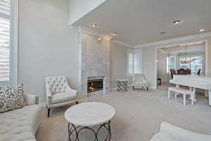 Living area featuring light carpet, baseboards, crown molding, a fireplace, and a notable chandelier