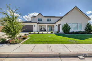 Modern farmhouse style home with driveway, a front lawn, an attached garage, and stucco siding