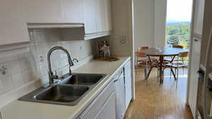 Kitchen featuring light wood finished floors, backsplash, stainless steel dishwasher, white cabinets, and a sink