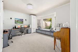 Home office with ornamental molding, light carpet, and built in study area