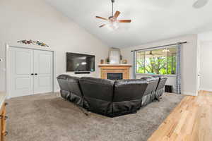 Living room featuring ceiling fan, high vaulted ceiling, a tiled fireplace, and baseboards