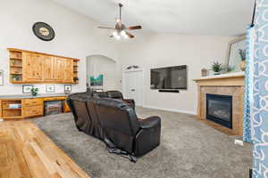 Living room featuring arched walkways, ceiling fan, high vaulted ceiling, a tile fireplace, and baseboards