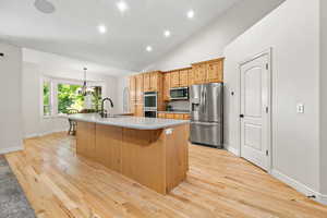 Kitchen featuring a center island with sink, stainless steel appliances, light countertops, light wood-type flooring, and a sink