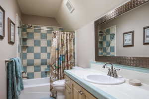 Bathroom with toilet, shower / tub combo, vanity, visible vents, and vaulted ceiling