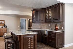 Bar with baseboards, a sink, backsplash, and a textured ceiling