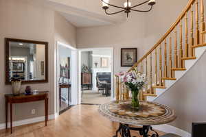 Foyer entrance with stairs, wood finished floors, a glass covered fireplace, and a chandelier