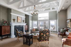 Living room with high vaulted ceiling, carpet floors, a high end fireplace, beamed ceiling, and an inviting chandelier