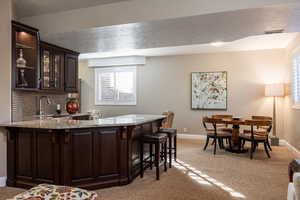 Bar with visible vents, baseboards, decorative backsplash, light colored carpet, and a sink