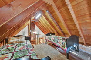 Carpeted bedroom with vaulted ceiling with beams and wood ceiling