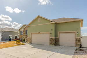 View of front facade with stone siding, driveway, an attached garage, and stucco siding