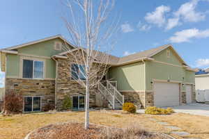 View of front of house with stucco siding, concrete driveway, an attached garage, stone siding, and stairs