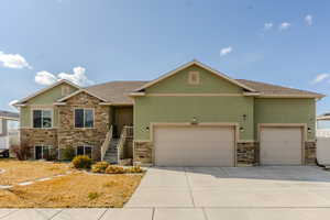 View of front facade with stucco siding, a shingled roof, a garage, stone siding, and driveway