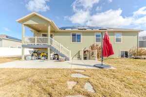 Back of property featuring a yard, a patio, solar panels, stucco siding, and a wooden deck