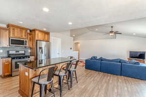 Kitchen with appliances with stainless steel finishes, arched walkways, light wood-style flooring, and lofted ceiling