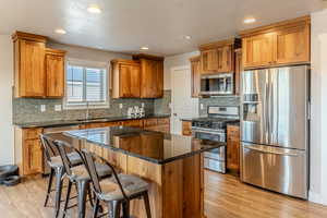 Kitchen with a breakfast bar area, light wood finished floors, stainless steel appliances, a sink, and a kitchen island