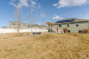 Back of house featuring stucco siding, a fenced backyard, solar panels, and a yard