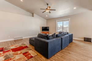 Living area with lofted ceiling, a ceiling fan, visible vents, baseboards, and light wood-type flooring