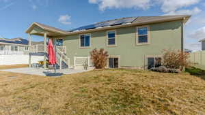 Back of house featuring a yard, a patio area, roof mounted solar panels, and stucco siding