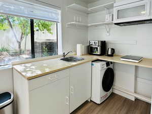 Kitchen featuring white microwave, a sink, wood finished floors, open shelves, and washer / clothes dryer