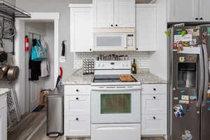 Kitchen featuring white appliances, white cabinetry, and decorative backsplash