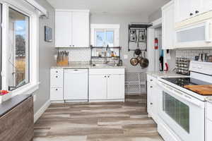 Kitchen with light stone counters, white appliances, white cabinets, and light wood finished floors