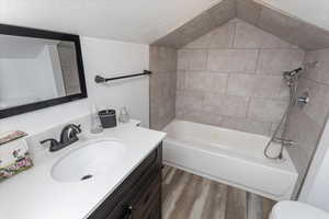 Bathroom with lofted ceiling, a textured ceiling, wood finished floors, vanity, and shower / bathing tub combination