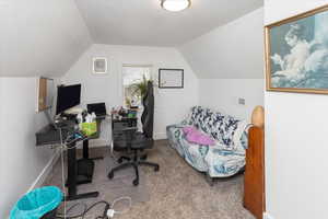 Carpeted home office featuring lofted ceiling, visible vents, a textured ceiling, and baseboards