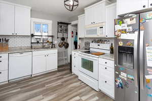 Kitchen with backsplash, white cabinets, a sink, light wood-type flooring, and white appliances