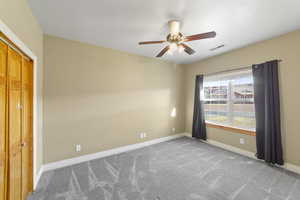 Carpeted spare room featuring visible vents, baseboards, and a ceiling fan