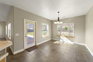 Unfurnished dining area with dark tile patterned flooring, visible vents, a notable chandelier, and baseboards