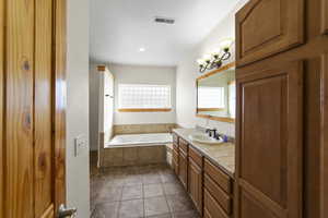 Full bathroom featuring tile patterned flooring, a garden tub, vanity, visible vents, and an inviting chandelier