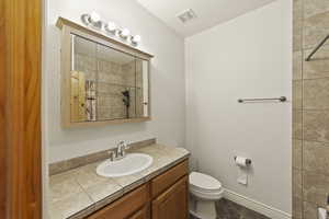 Full bath with visible vents, toilet, vanity, tiled shower, and baseboards