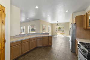 Kitchen with baseboards, brown cabinetry, a peninsula, hanging light fixtures, and stainless steel appliances