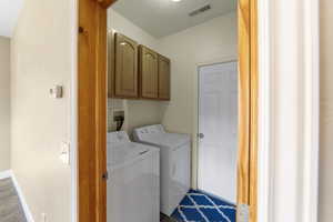 Laundry room featuring cabinet space, visible vents, wood finished floors, washer and dryer, and baseboards