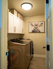 Washroom featuring visible vents, baseboards, cabinet space, light wood finished floors, and washing machine and clothes dryer