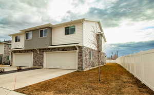 Back view of Townhome / multi-family property featuring stone siding, concrete driveway, fence, and a garage