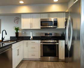 Kitchen with wood finish floors, stainless steel appliances, white cabinetry, a sink, and dark stone countertops