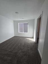 Empty room featuring a textured ceiling, dark carpet, and baseboards