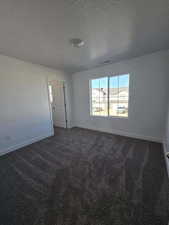 Unfurnished room featuring dark colored carpet, a textured ceiling, and baseboards