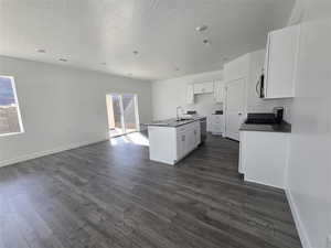 Kitchen with white cabinets, dark countertops, appliances with stainless steel finishes, open floor plan, and dark wood-style flooring