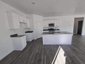 Kitchen featuring a center island with sink, stainless steel appliances, dark wood-type flooring, white cabinetry, and a textured ceiling