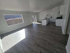 Interior space featuring dark wood-type flooring, a kitchen island with sink, open floor plan, and white cabinetry