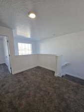 Empty room featuring a textured ceiling, dark colored carpet, and baseboards