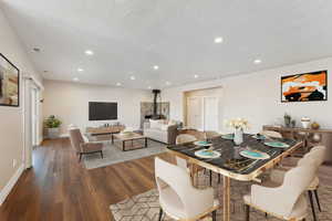 Dining space featuring wood finished floors, recessed lighting, a textured ceiling, baseboards, and a wood stove