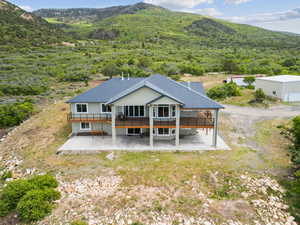 Rear view of house with a deck with mountain view, a patio, and a wooded view